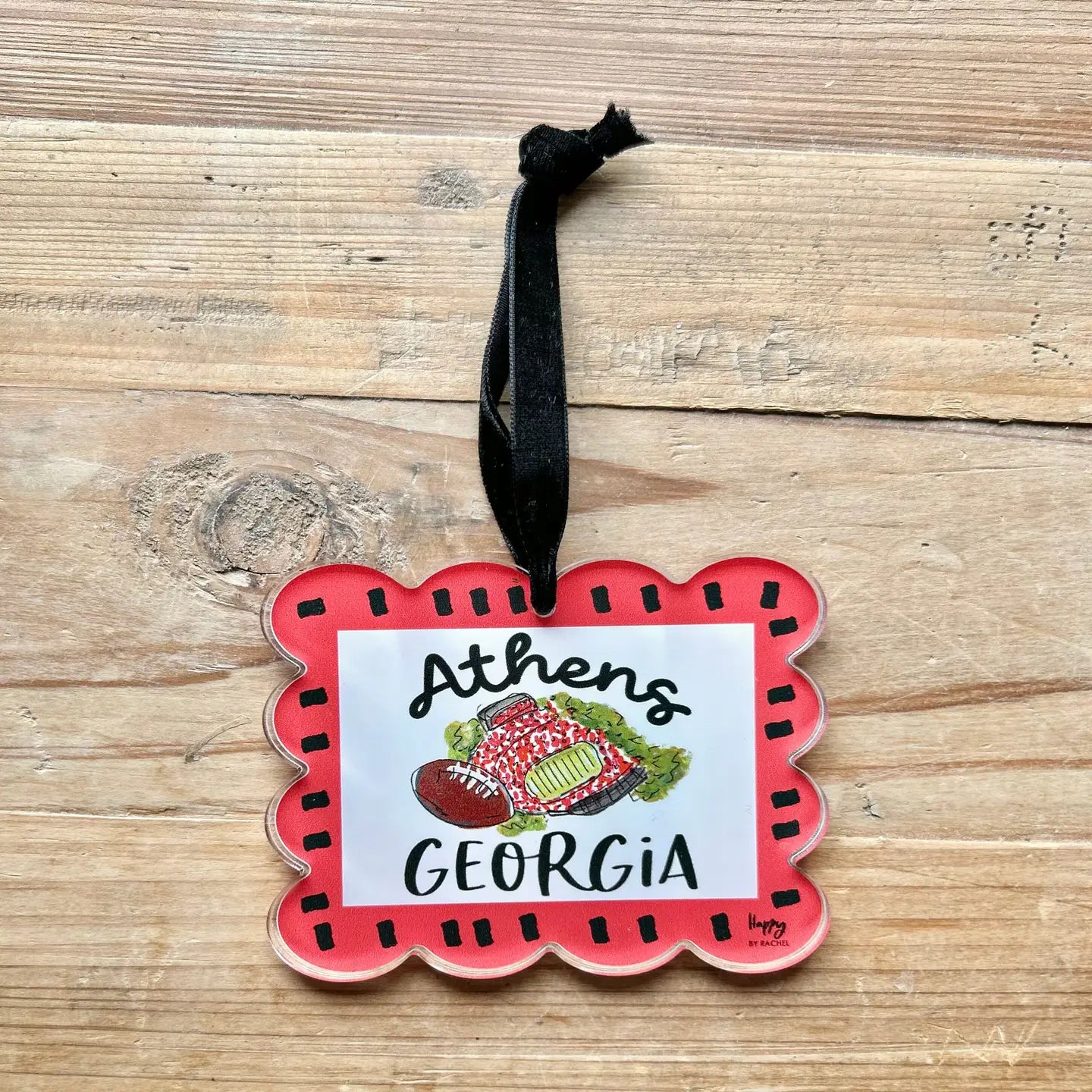 A scalloped acrylic ornament featuring a red border, a white center, and a hand-drawn illustration of a football and Sanford Stadium