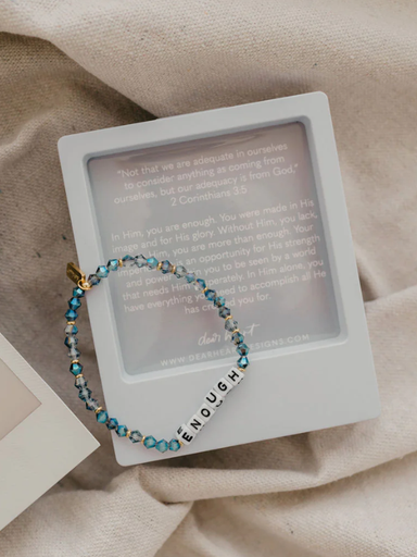 Bracelet with 'enough' charm on a white card with text, on a beige fabric background