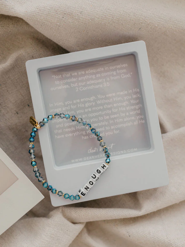 Bracelet with 'enough' charm on a white card with text, on a beige fabric background