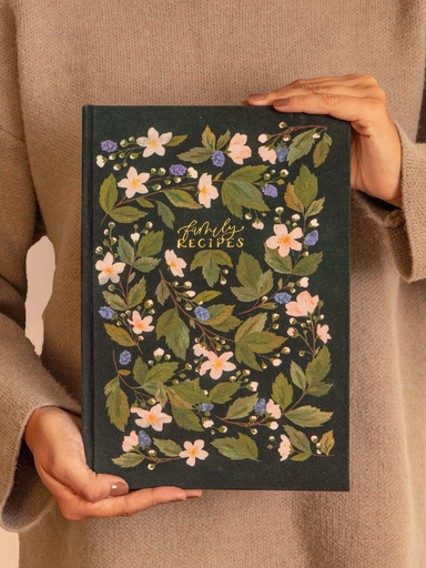 Book titled 'Family Recipes' with floral design held by a person wearing a beige sweater.
