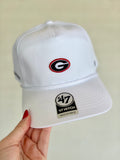 A white structured baseball cap held by a hand, featuring a Georgia Bulldogs logo patch on the front 