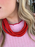 A person wearing a pink sweater and a red cotton roping necklace with a ball-and-eye closure.