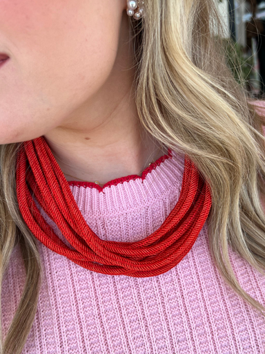 A person wearing a pink sweater and a red cotton roping necklace with a ball-and-eye closure.