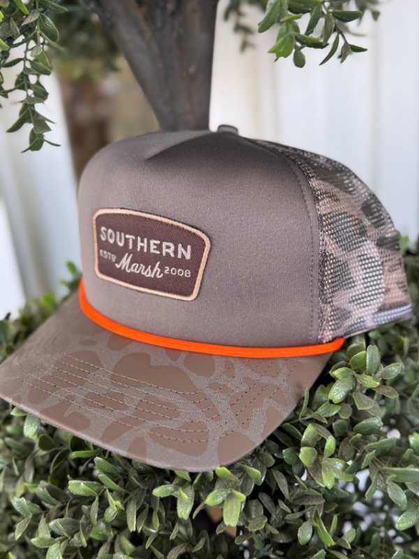 A retro camo pintail trucker hat in light brown with an orange snap closure and a Southern Marsh logo on the front.