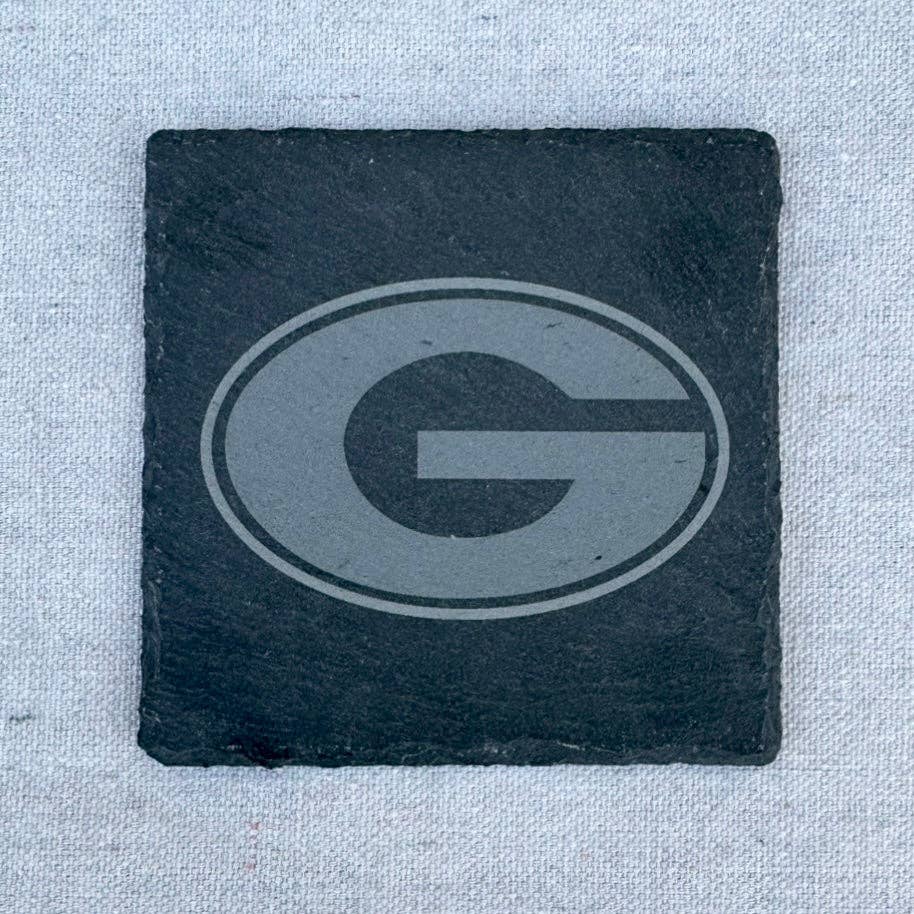 A square black slate coaster featuring a debossed gray Georgia Bulldogs 'G' logo, set against a light gray textured fabric background.