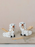 Two ceramic dog-shaped holders with sticks on a wooden surface.