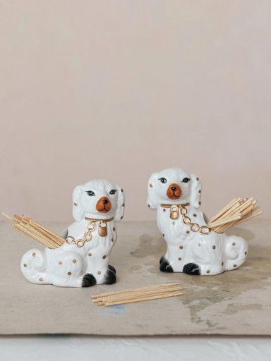 Two ceramic dog-shaped holders with sticks on a wooden surface.