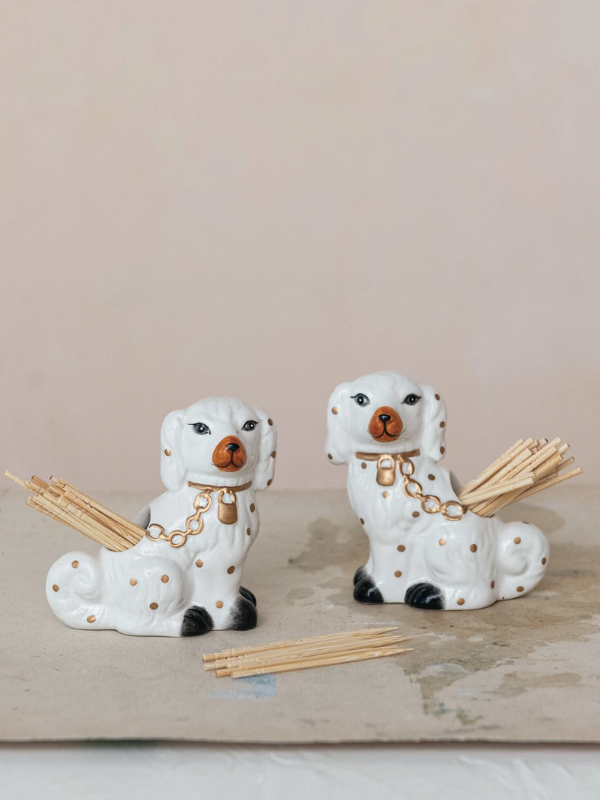 Two ceramic dog-shaped holders with sticks on a wooden surface.