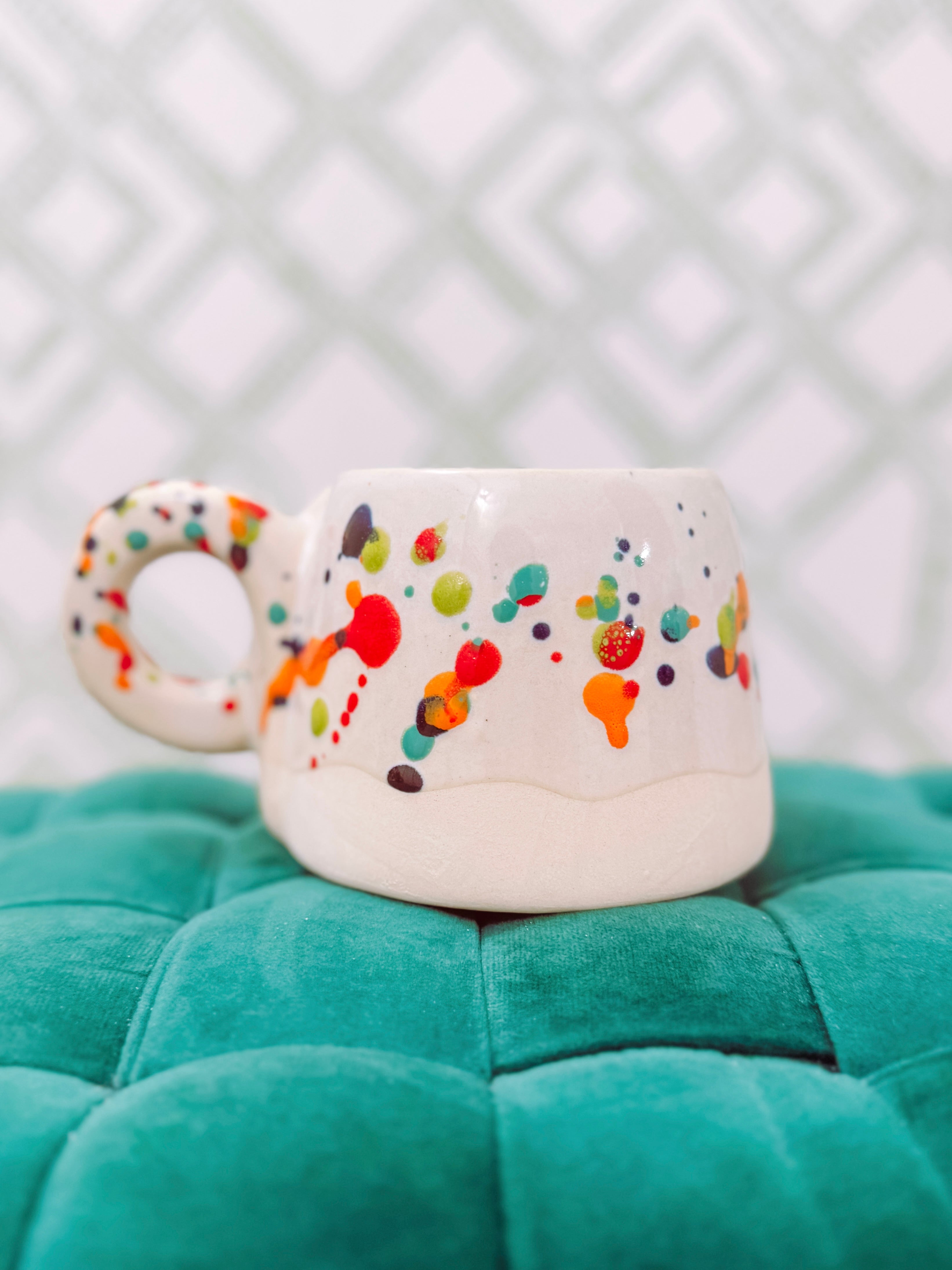 A white ceramic mug with a colorful splatter dot pattern and a loop handle.