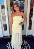 Butter-yellow strapless maxi dress featuring a fitted silhouette with a flowing gauzy hem panel, styled with gold jewelry for an elegant summer occasion look.