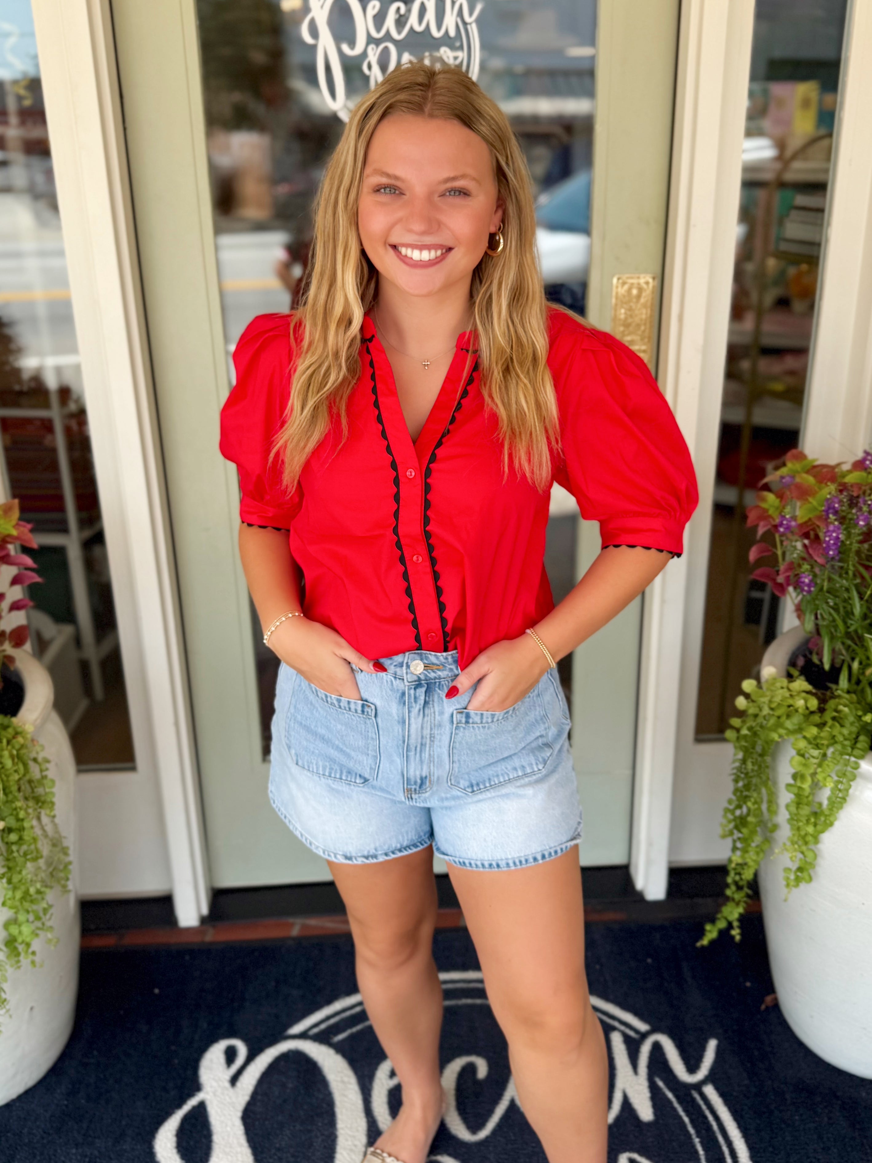 A red short-sleeve blouse with puff sleeves and a black trim ruffle front detailing. 