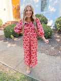 This midi dress features a bold rust and pink statement print with feminine ruffle detailing along the neckline and bodice.