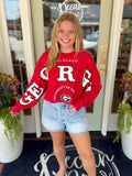 A red long-sleeve sweatshirt with large white 'Georgia' lettering and a University of Georgia logo.