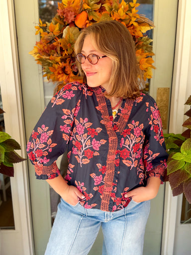  This navy top features a vibrant floral print in shades of pink, red, and coral with delicate ruffle trim along the neckline and front. 