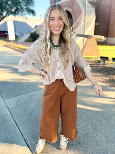 The Kat Eyelet Top in Taupe features a collared neckline, button-front design, and cuffed sleeves for an effortlessly polished look. 
