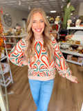 This cozy knit features an eye-catching abstract pattern in warm red and deep green against a soft oatmeal background.