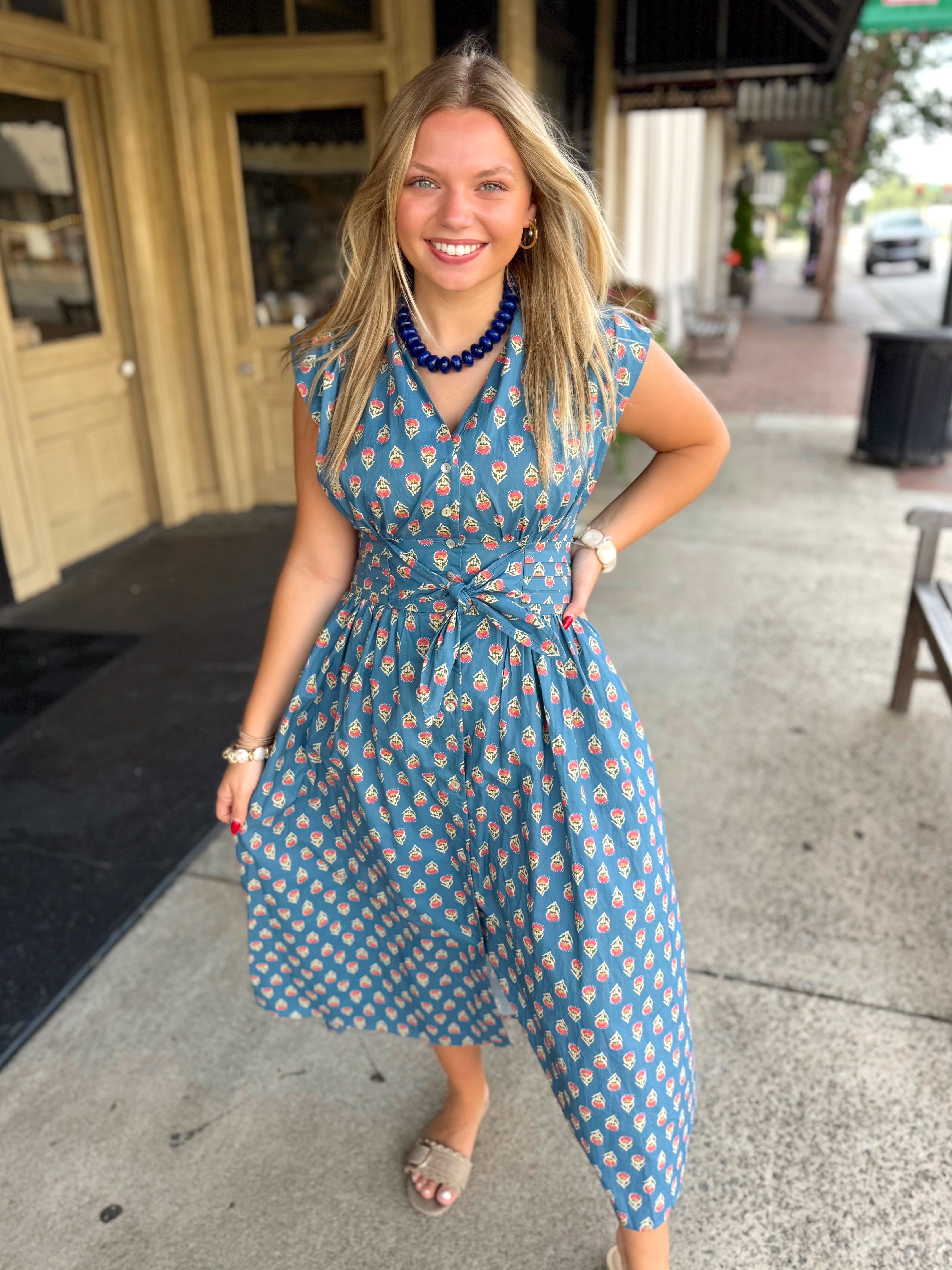 A blue midi dress with a floral pattern, a V-neck, and a tie waist.
