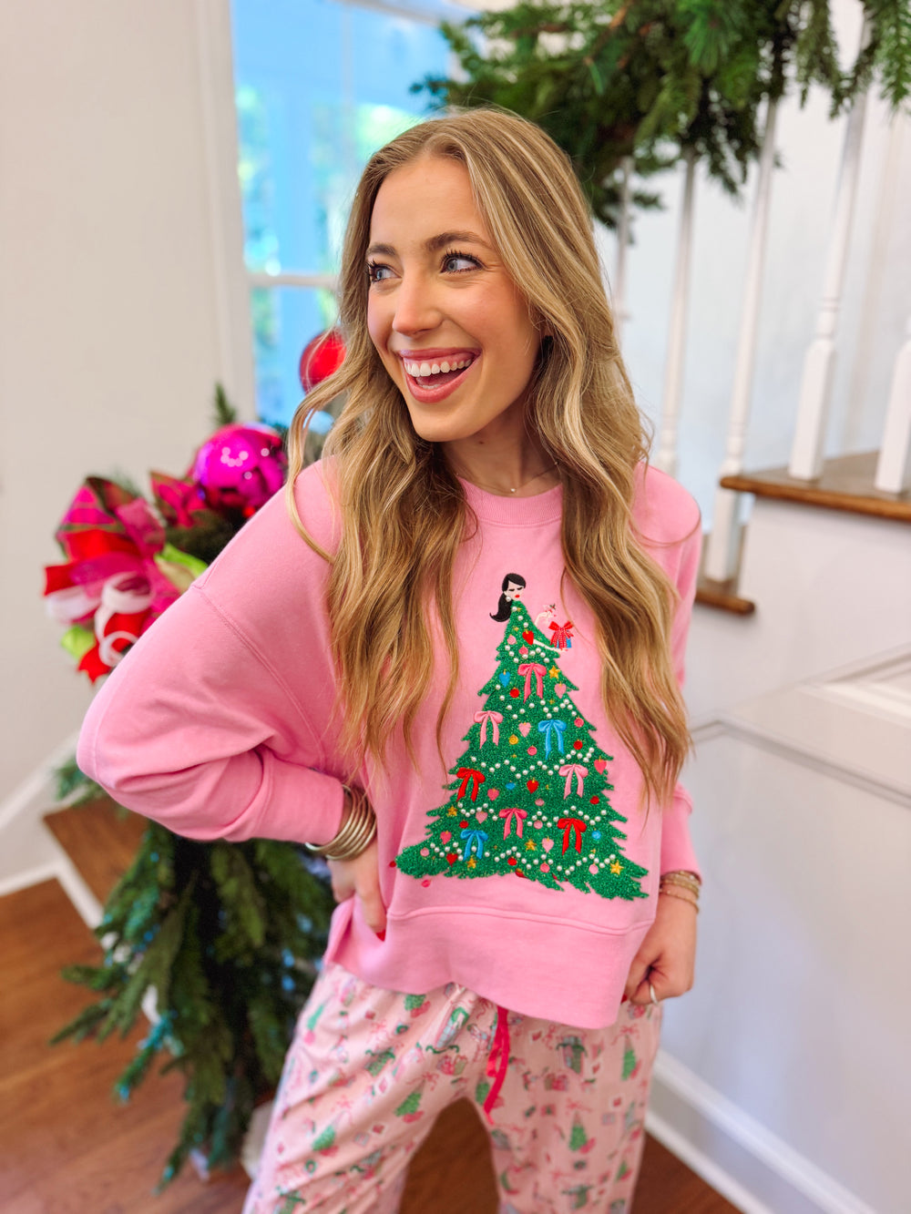 pink sweatshirt with a Christmas tree and a lady decorating it