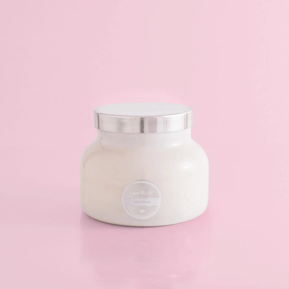 A volcano scented white candle in a white jar with a silver by capri blue.