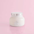 A volcano scented white candle in a white jar with a silver by capri blue.