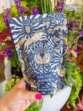 A hand with bright pink nail polish holds a stand-up pouch of Morro Snack Salted Cashews. The pouch features a navy blue background with a gold foil pattern of a tiger and zebra stripes.