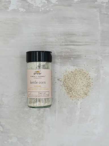 Bottle of Finch + Fennel Kettle Corn Seasoning beside a pile of seasoning blend, featuring cane sugar, sea salt, brown butter, and vanilla bean for sweet-and-salty gourmet popcorn.
